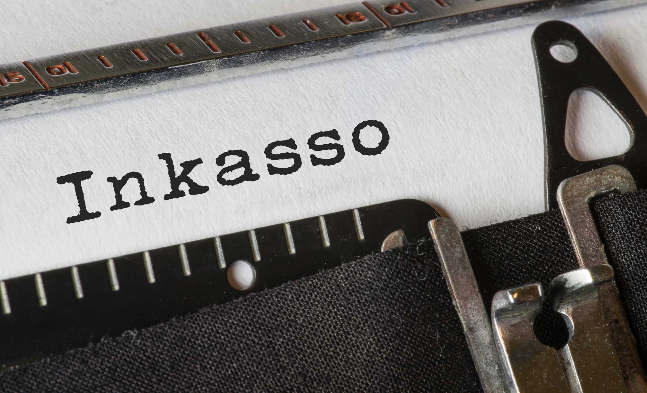 Schreibmaschine tippt das Wort Inkasso. Symbolbild für das Beauftragen eines Inkassounternehmens im Forderungsmanagement.